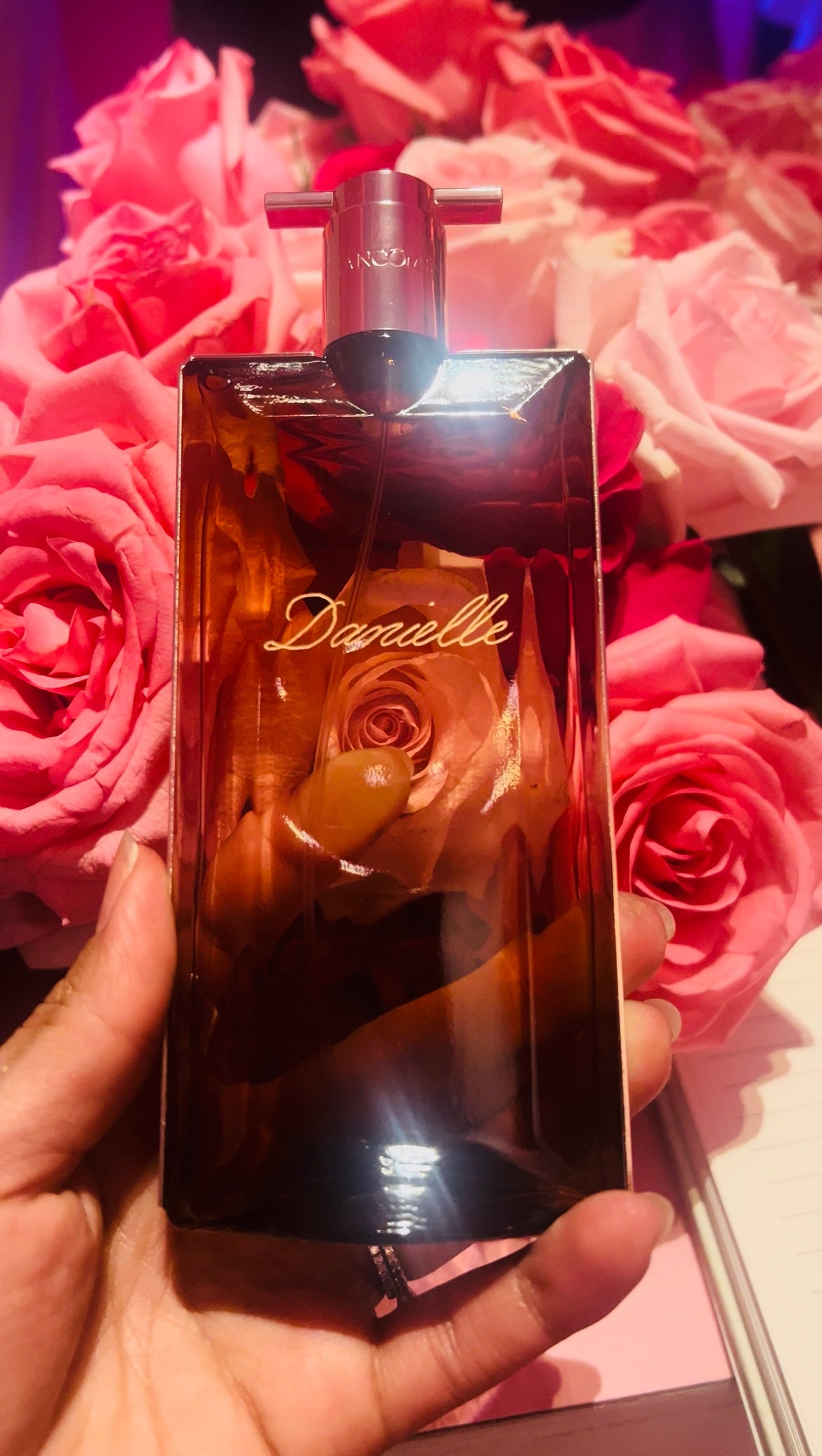 Perfume bottle held in front of pink flowers